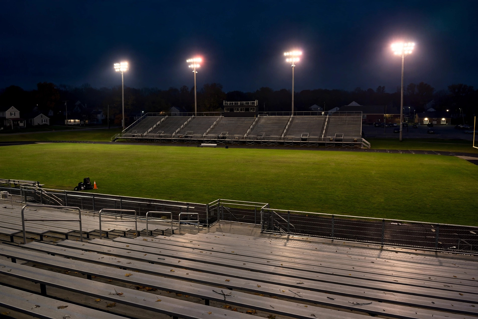Editorial illustration: a small-town high school football stadium at night under floodlights